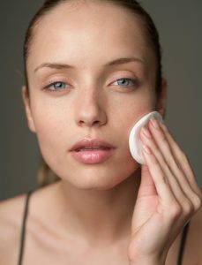 Young woman using a cotton pad for skincare, highlighting beauty routine.